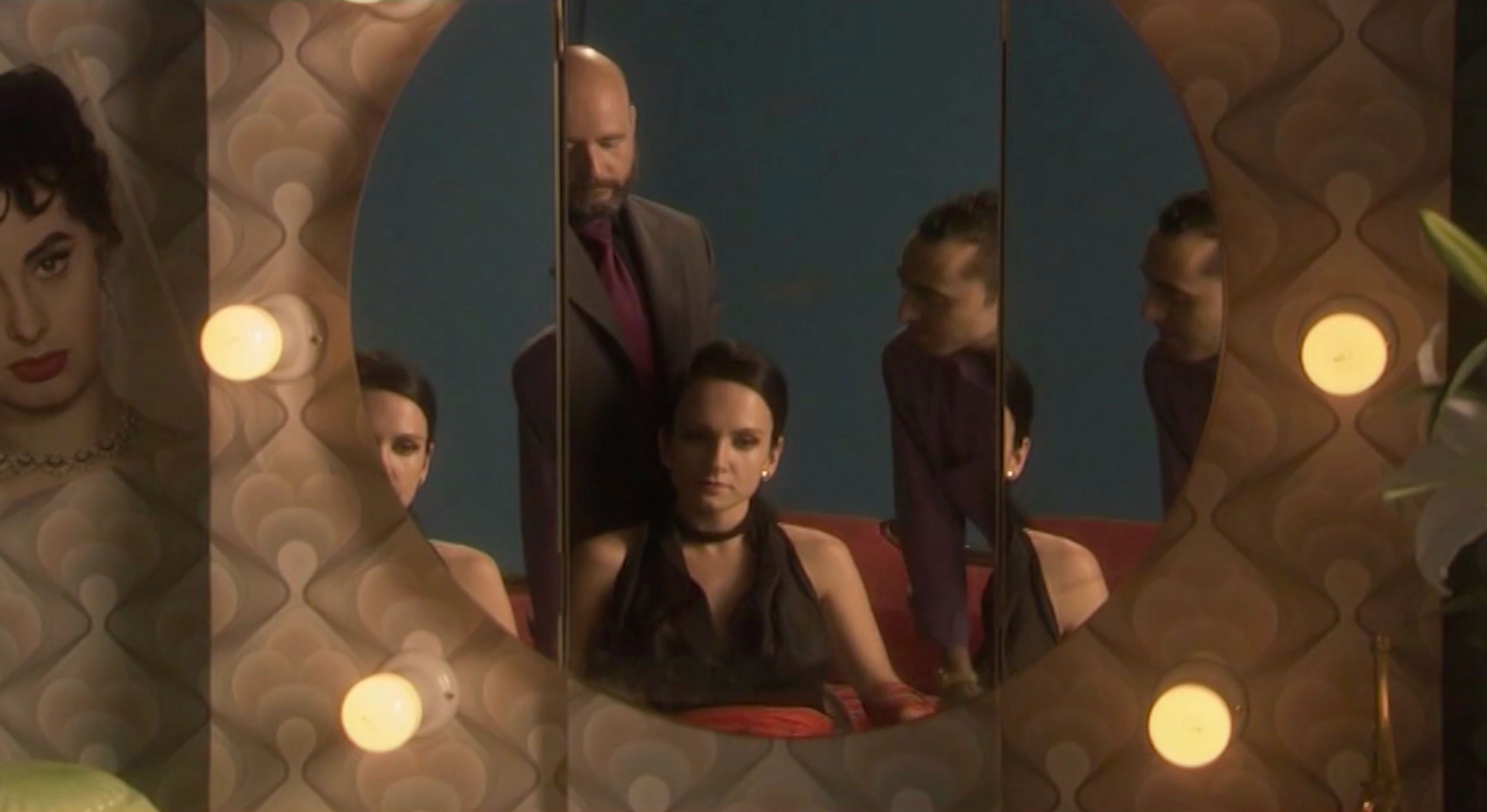 Noir style dressing room circular mirror fractures the image of three repeating characters in a tense scene