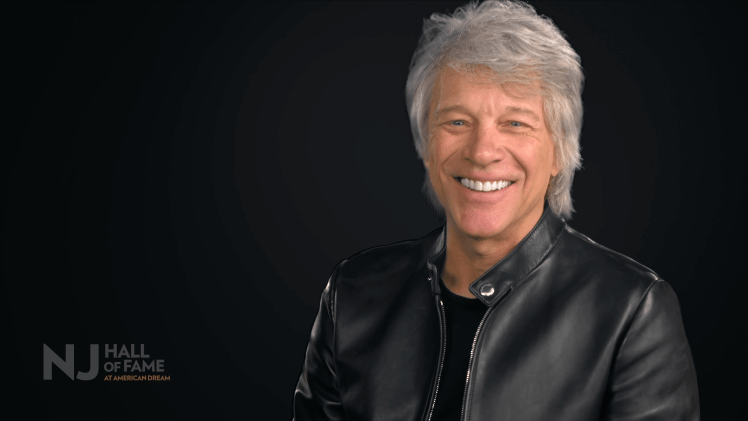 Musician Jon Bon Jovi headshot smiling on a black background with logo of the New Jersey Hall of Fame